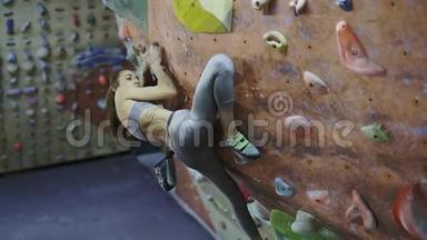 年轻女子攀岩者正在攀岩健身房里攀岩。 苗条美丽的女人在室内攀岩墙上锻炼